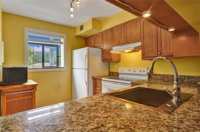 kitchen with track lighting, sink, white appliances, and dark stone countertops