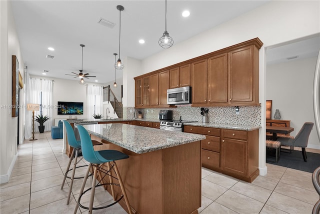 kitchen with ceiling fan, light stone counters, kitchen peninsula, a breakfast bar area, and appliances with stainless steel finishes