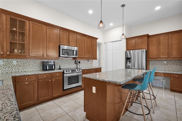 kitchen featuring a center island, stainless steel appliances, light stone counters, pendant lighting, and decorative backsplash