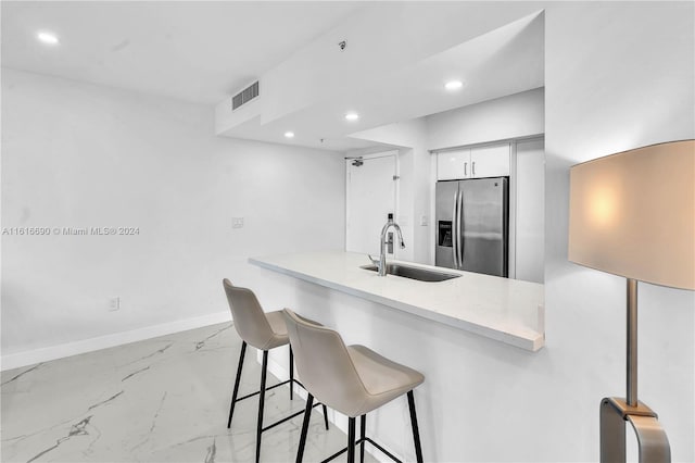 kitchen featuring light stone counters, white cabinets, stainless steel fridge, sink, and a breakfast bar area