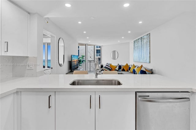 kitchen with white cabinets, sink, stainless steel dishwasher, light stone counters, and kitchen peninsula