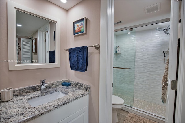 bathroom featuring a shower with door, vanity, and toilet