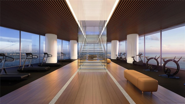 workout area featuring a water view, wood-type flooring, and a wall of windows