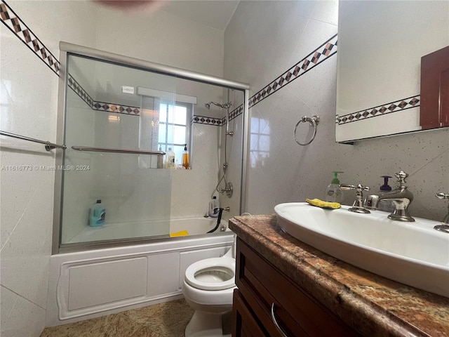 full bathroom featuring vanity, tile walls, bath / shower combo with glass door, and toilet