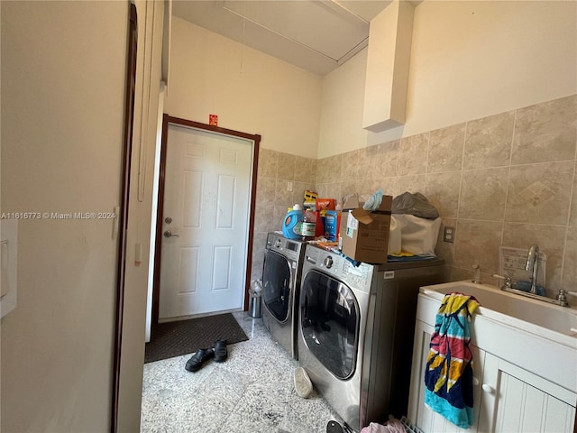 clothes washing area featuring washing machine and clothes dryer, tile patterned floors, and tile walls