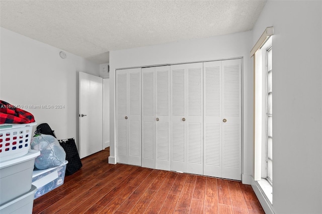 unfurnished bedroom with a textured ceiling, dark wood-type flooring, multiple windows, and a closet