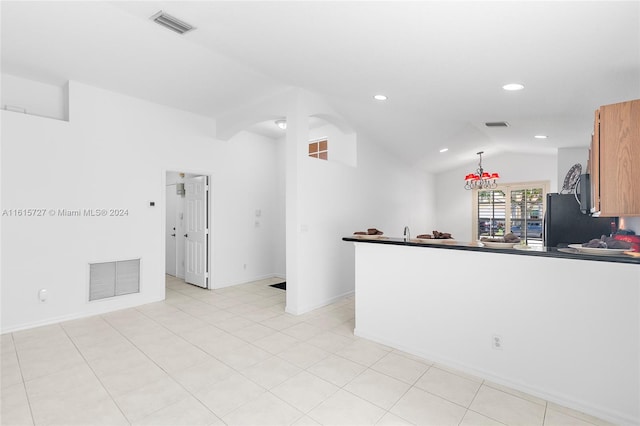 kitchen with light tile patterned flooring, vaulted ceiling, kitchen peninsula, black refrigerator, and decorative light fixtures