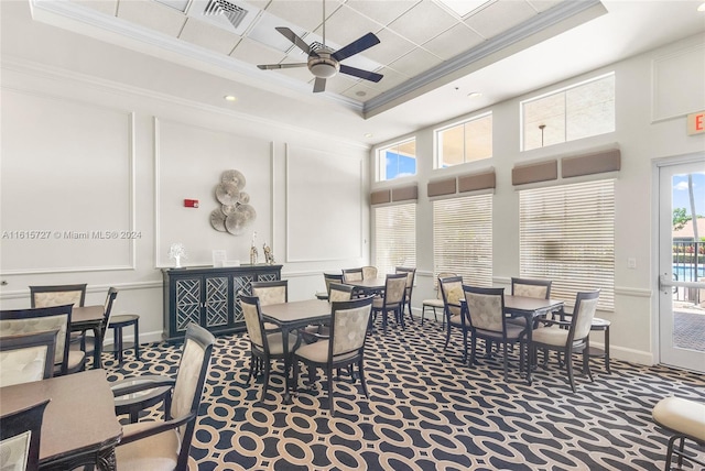 dining area featuring ceiling fan, a high ceiling, a tray ceiling, crown molding, and dark carpet