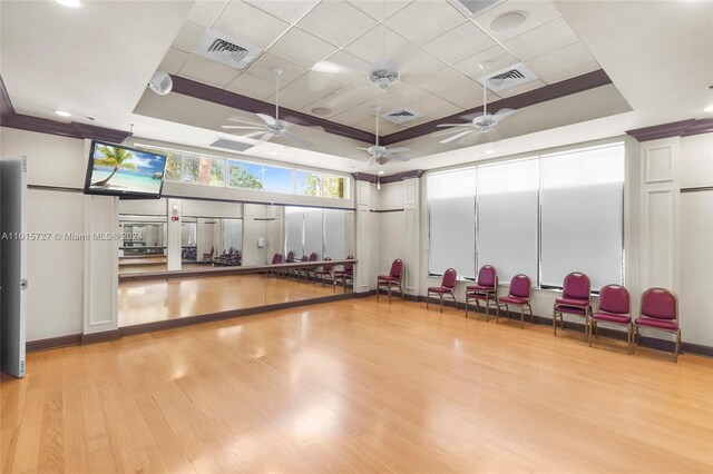 exercise area featuring light hardwood / wood-style flooring, ceiling fan, and a raised ceiling