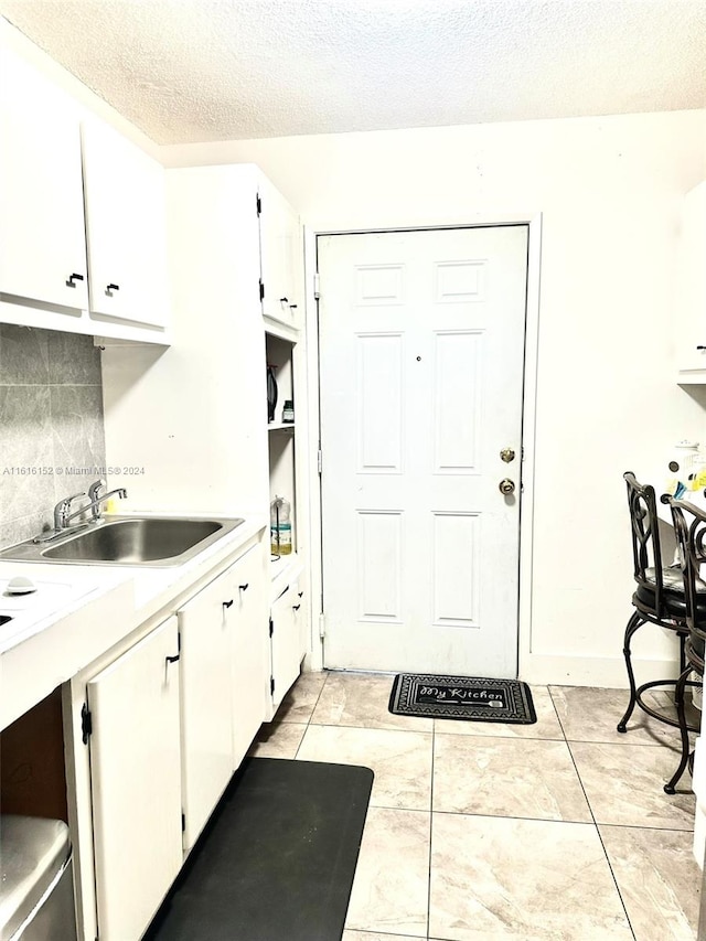 kitchen featuring sink, tasteful backsplash, a textured ceiling, light tile patterned floors, and white cabinets