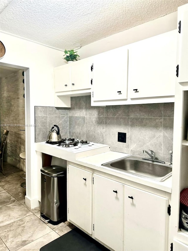 kitchen with backsplash, sink, a textured ceiling, white cabinets, and light tile patterned floors