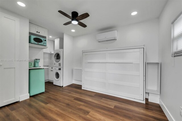 washroom featuring dark hardwood / wood-style flooring, an AC wall unit, stacked washer / dryer, and ceiling fan