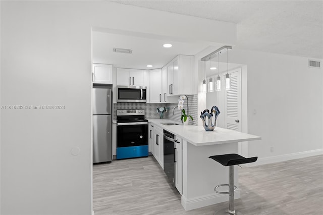 kitchen with sink, appliances with stainless steel finishes, white cabinetry, hanging light fixtures, and a kitchen bar