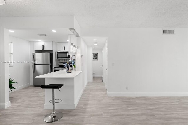 kitchen featuring a textured ceiling, a breakfast bar area, white cabinets, and appliances with stainless steel finishes