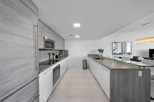 kitchen with light tile patterned flooring, sink, wall oven, black electric stovetop, and white cabinets