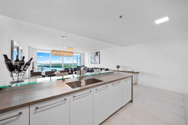 kitchen with pendant lighting, butcher block counters, sink, white cabinets, and expansive windows