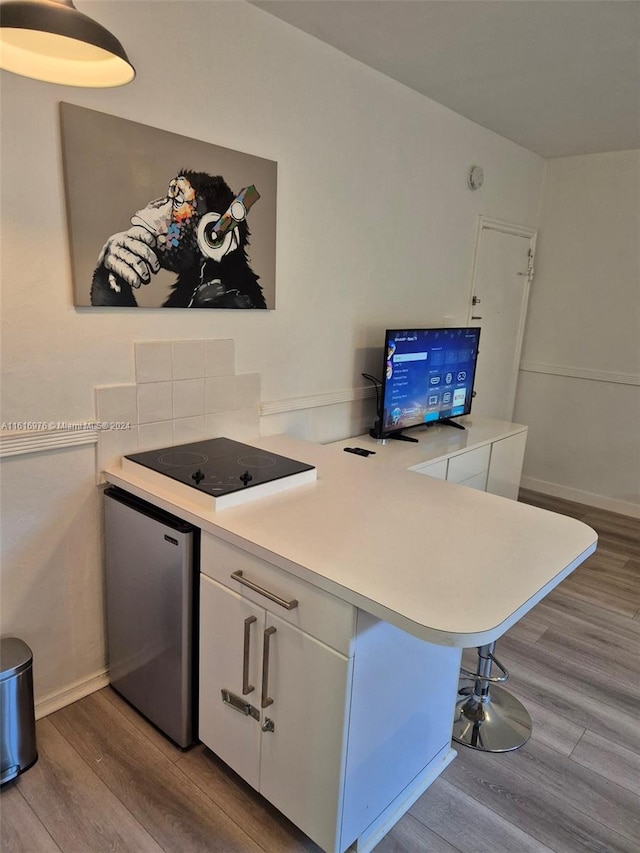 kitchen with light hardwood / wood-style floors, kitchen peninsula, white cabinetry, a kitchen breakfast bar, and stainless steel fridge