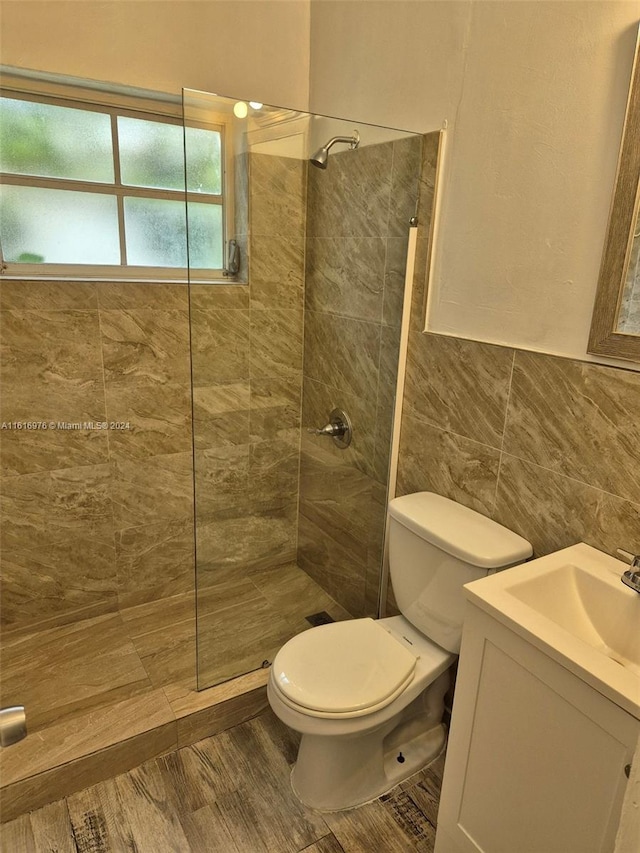 bathroom with toilet, vanity, tile walls, and a tile shower