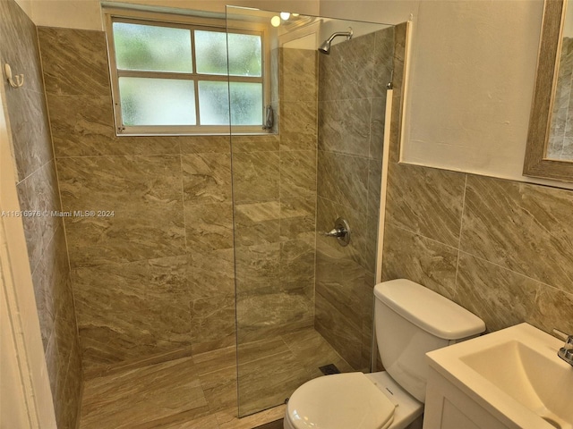 bathroom with tile walls, toilet, vanity, and a tile shower