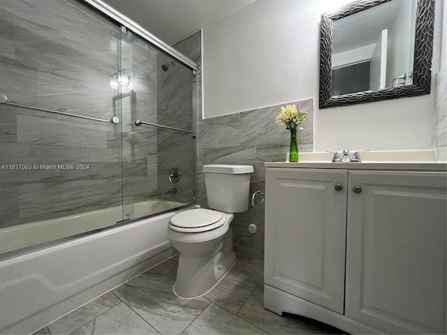 full bathroom with shower / bath combination with glass door, vanity, tile walls, and toilet