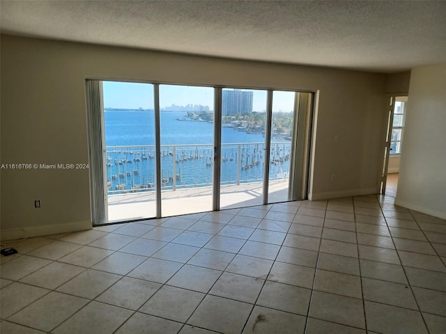 tiled spare room featuring a water view and a textured ceiling