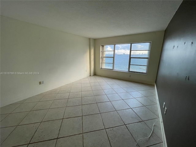 unfurnished room with a water view, a textured ceiling, and light tile patterned floors