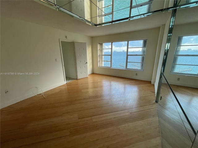 spare room featuring a water view, a towering ceiling, and light hardwood / wood-style floors