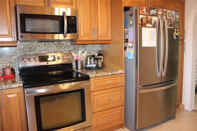 kitchen with decorative backsplash, light stone countertops, appliances with stainless steel finishes, and light tile patterned floors