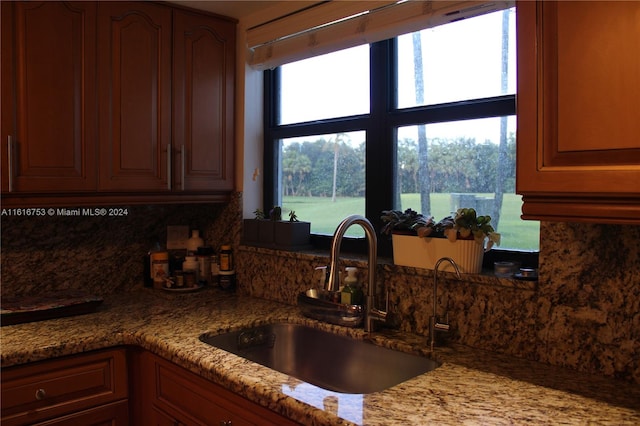 kitchen featuring backsplash, sink, light stone countertops, and a healthy amount of sunlight