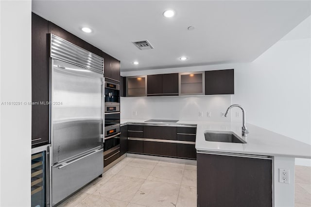 kitchen with sink, dark brown cabinetry, built in refrigerator, light tile patterned floors, and beverage cooler