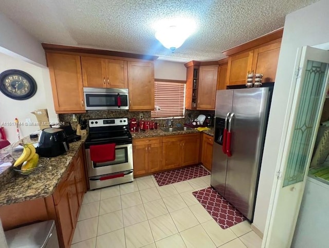 kitchen with sink, dark stone counters, appliances with stainless steel finishes, light tile patterned floors, and backsplash