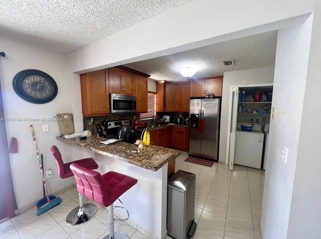 kitchen with stainless steel appliances, a breakfast bar, kitchen peninsula, dark stone counters, and backsplash