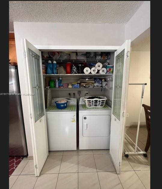 clothes washing area with light tile patterned flooring, independent washer and dryer, and a textured ceiling