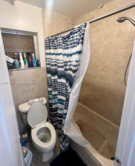 bathroom with tile walls, toilet, and shower / tub combo with curtain