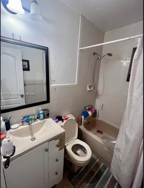 full bathroom featuring vanity, tile walls, toilet, and shower / bathtub combination with curtain