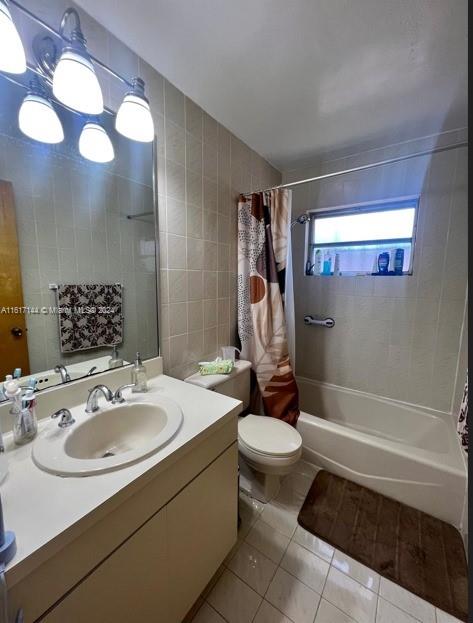 full bathroom featuring vanity, shower / bath combo with shower curtain, tile walls, tile patterned floors, and toilet