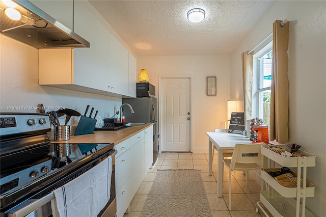 kitchen with white cabinets, light tile patterned floors, a textured ceiling, stainless steel range with electric stovetop, and wall chimney exhaust hood