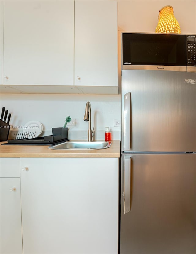 kitchen with sink, stainless steel fridge, and white cabinetry