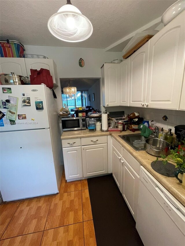 kitchen with white appliances, sink, decorative light fixtures, light wood-type flooring, and white cabinetry