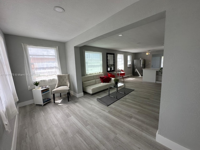 living room featuring ceiling fan, light wood-type flooring, a textured ceiling, and a wealth of natural light