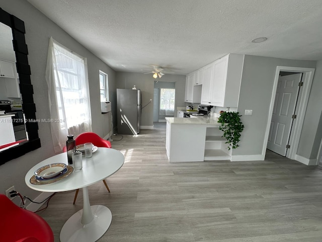 kitchen with kitchen peninsula, appliances with stainless steel finishes, a textured ceiling, white cabinets, and light wood-type flooring