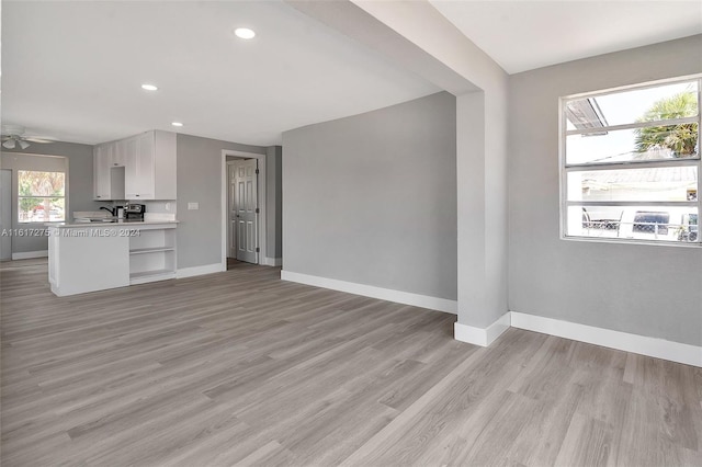 unfurnished living room with ceiling fan, plenty of natural light, sink, and light wood-type flooring