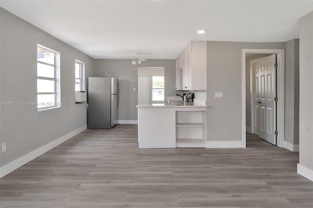 kitchen with white cabinetry, ceiling fan, kitchen peninsula, stainless steel fridge, and light wood-type flooring