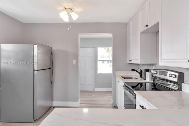 kitchen with sink, light wood-type flooring, light stone counters, white cabinetry, and stainless steel appliances