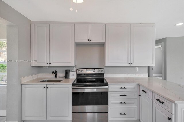 kitchen with light stone countertops, white cabinetry, stainless steel range with electric stovetop, and sink