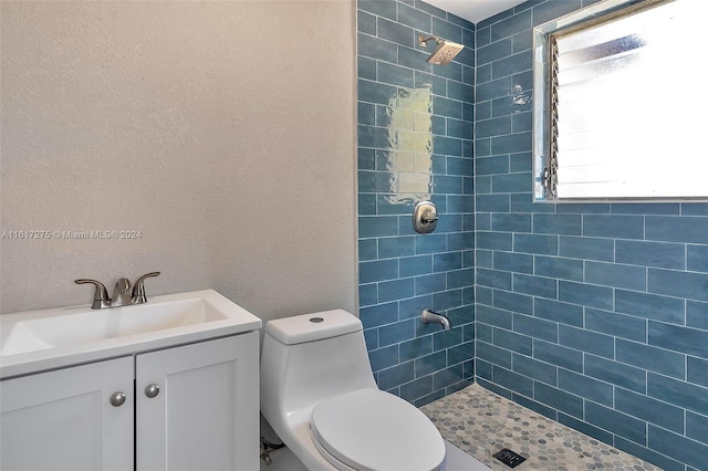 bathroom with a tile shower, vanity, and toilet