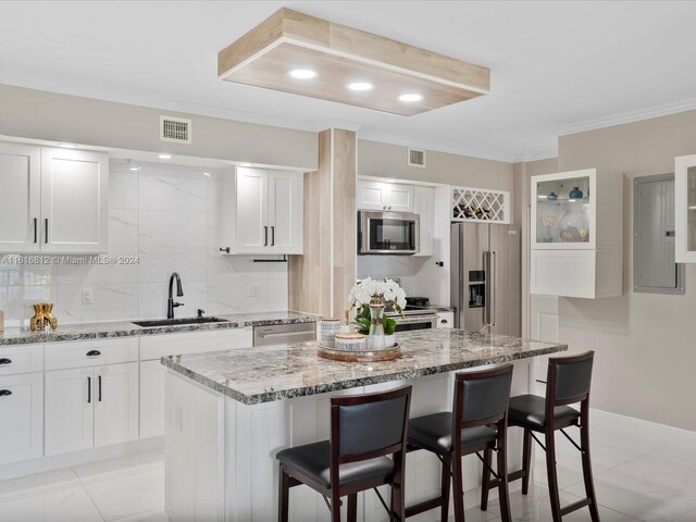 kitchen featuring a center island, sink, appliances with stainless steel finishes, white cabinetry, and a breakfast bar area