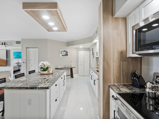 kitchen featuring stainless steel appliances, a kitchen island, a kitchen breakfast bar, dark stone counters, and white cabinets