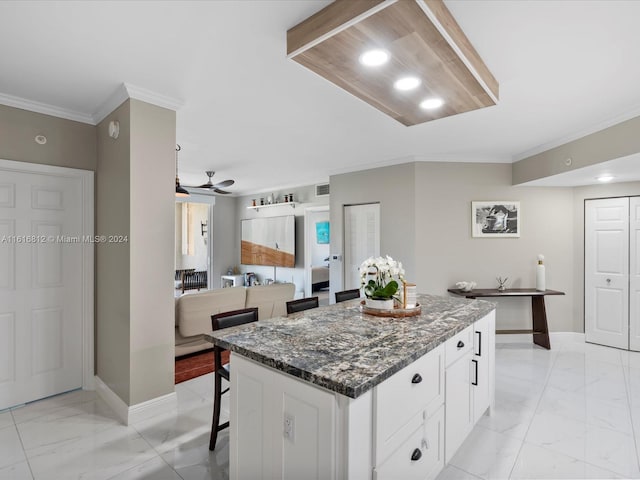 kitchen featuring ceiling fan, a center island, dark stone countertops, a breakfast bar area, and white cabinets