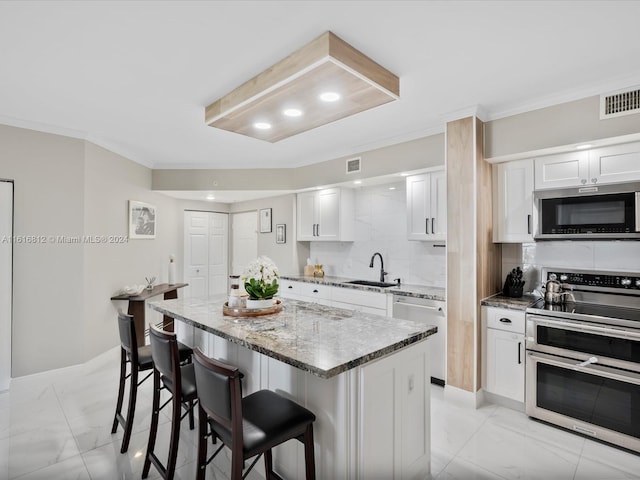 kitchen featuring light stone countertops, a kitchen island, a kitchen breakfast bar, white cabinets, and appliances with stainless steel finishes